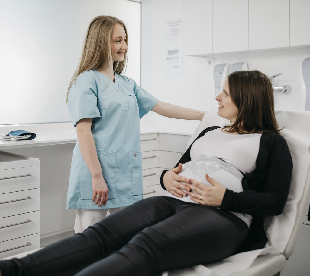 Krankenschwester im Gespräch mit einer schwangeren Frau auf dem Untersuchungsliege